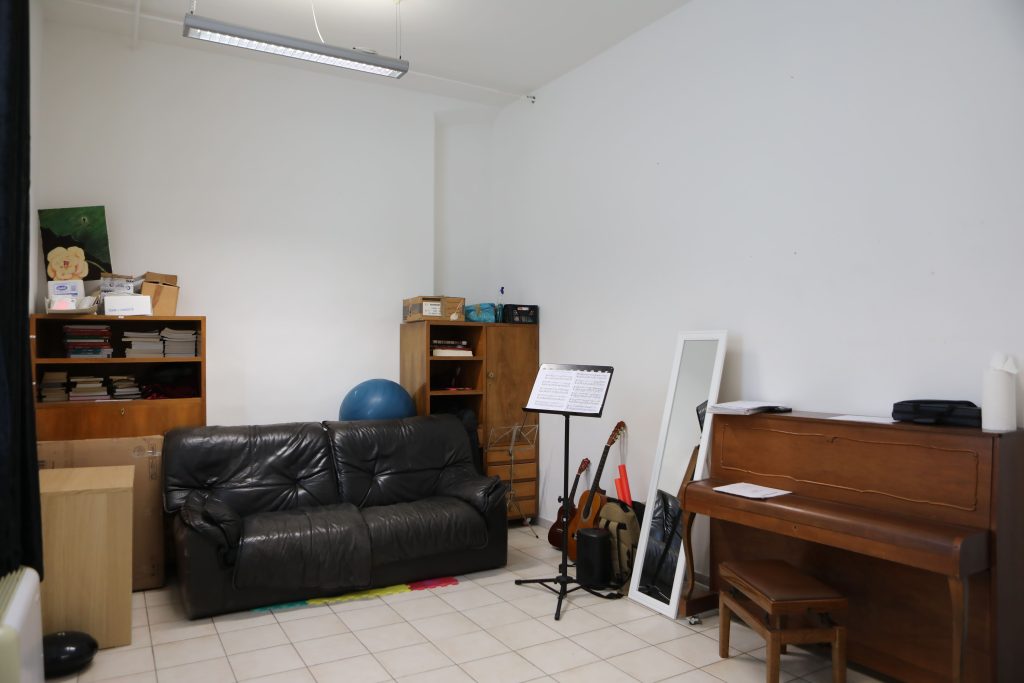 stanza con all'interno un divano nero, un leggio, uno specchio, un pianoforte
