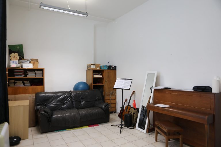 stanza con all'interno un divano nero, un leggio, uno specchio, un pianoforte
